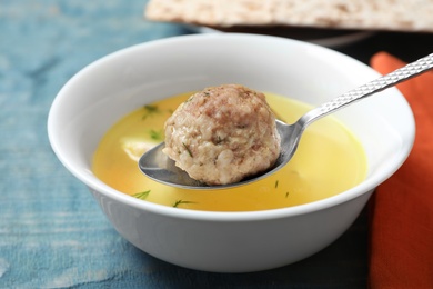 Photo of Spoon with matzoh ball over bowl of soup on table, closeup. Jewish cuisine