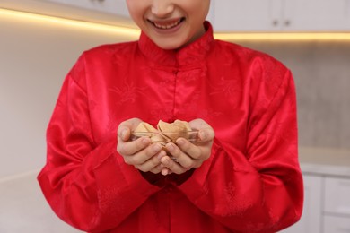 Young woman holding bowl of tasty fortune cookies with predictions in kitchen, closeup