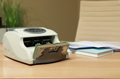 Photo of Modern banknote counter with money on wooden table indoors. Space for text