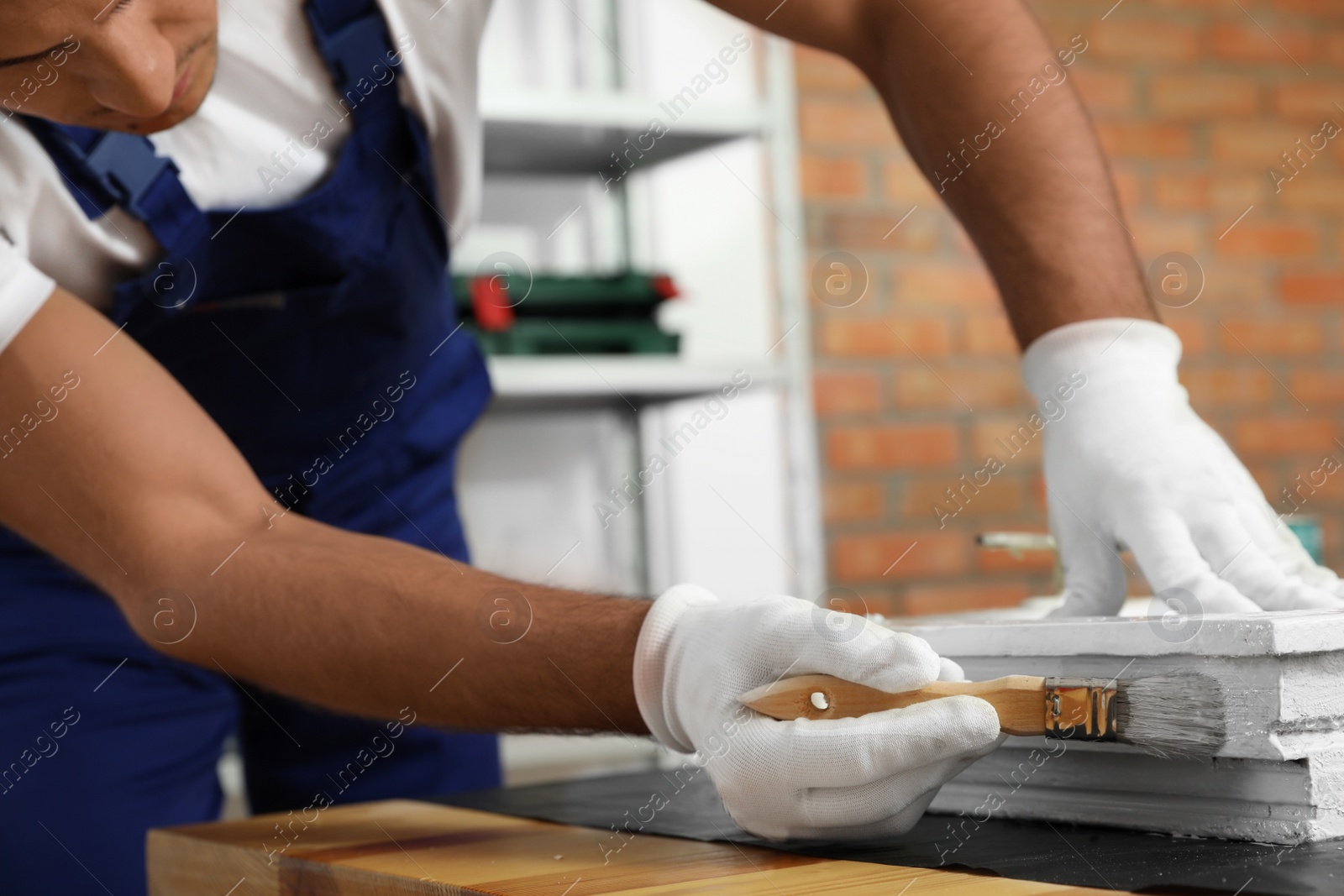 Photo of Repairman painting old window at table indoors, closeup