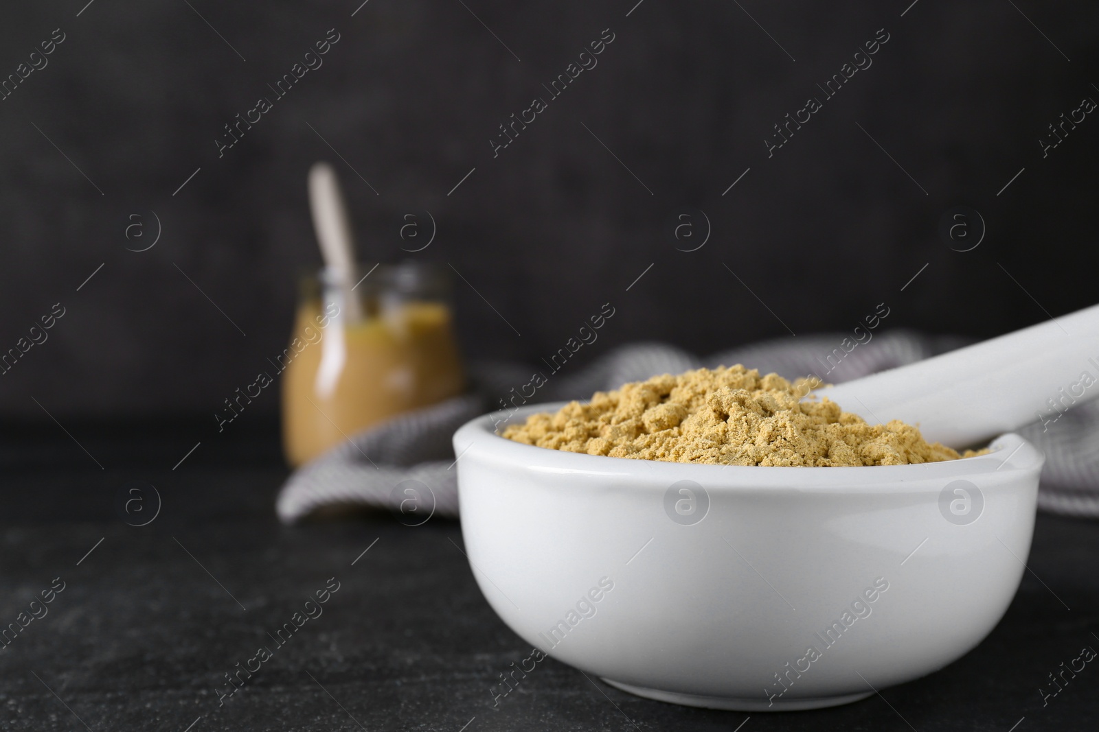 Photo of Mortar with mustard powder on black table. Space for text