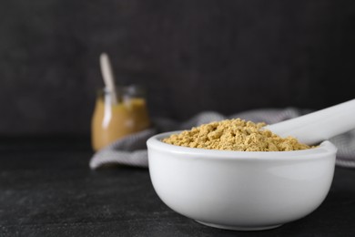 Photo of Mortar with mustard powder on black table. Space for text