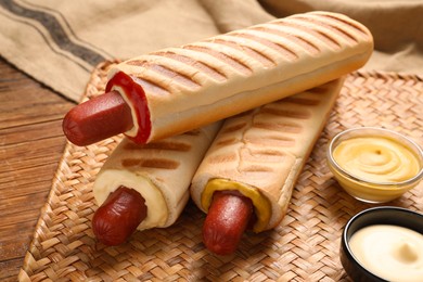 Photo of Tasty french hot dogs and dip sauces on wooden table, closeup