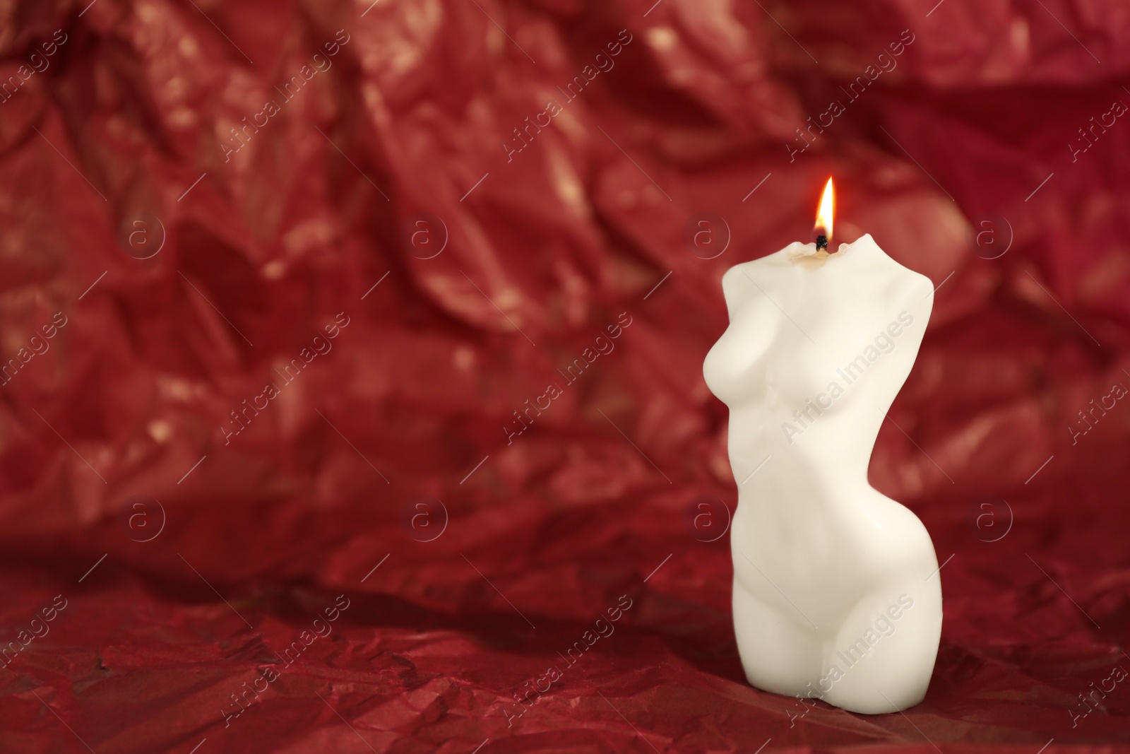 Photo of Beautiful burning female body shaped candle on red crumpled parchment. Space for text