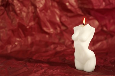 Photo of Beautiful burning female body shaped candle on red crumpled parchment. Space for text