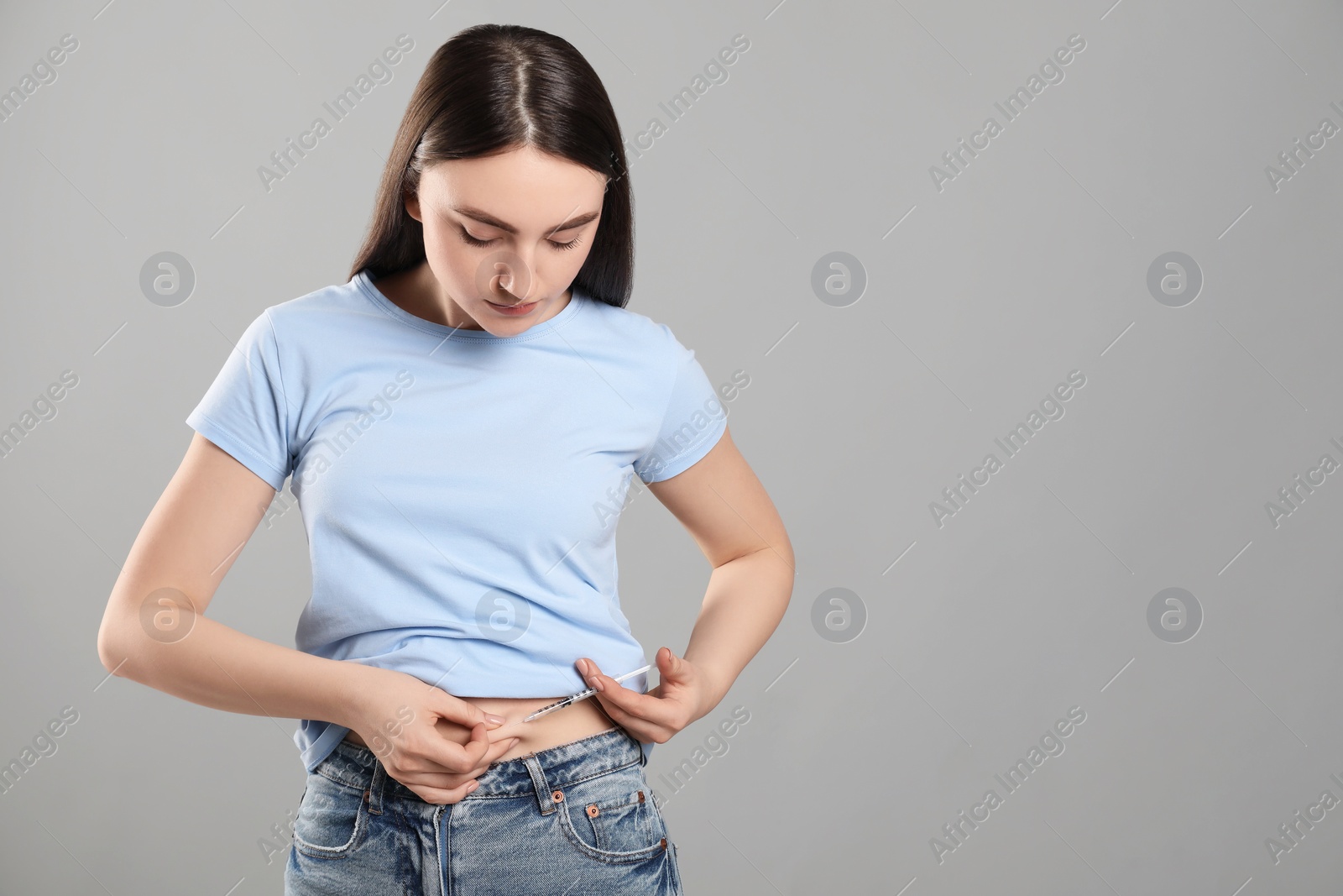 Photo of Diabetes. Woman making insulin injection into her belly on grey background. Space for text