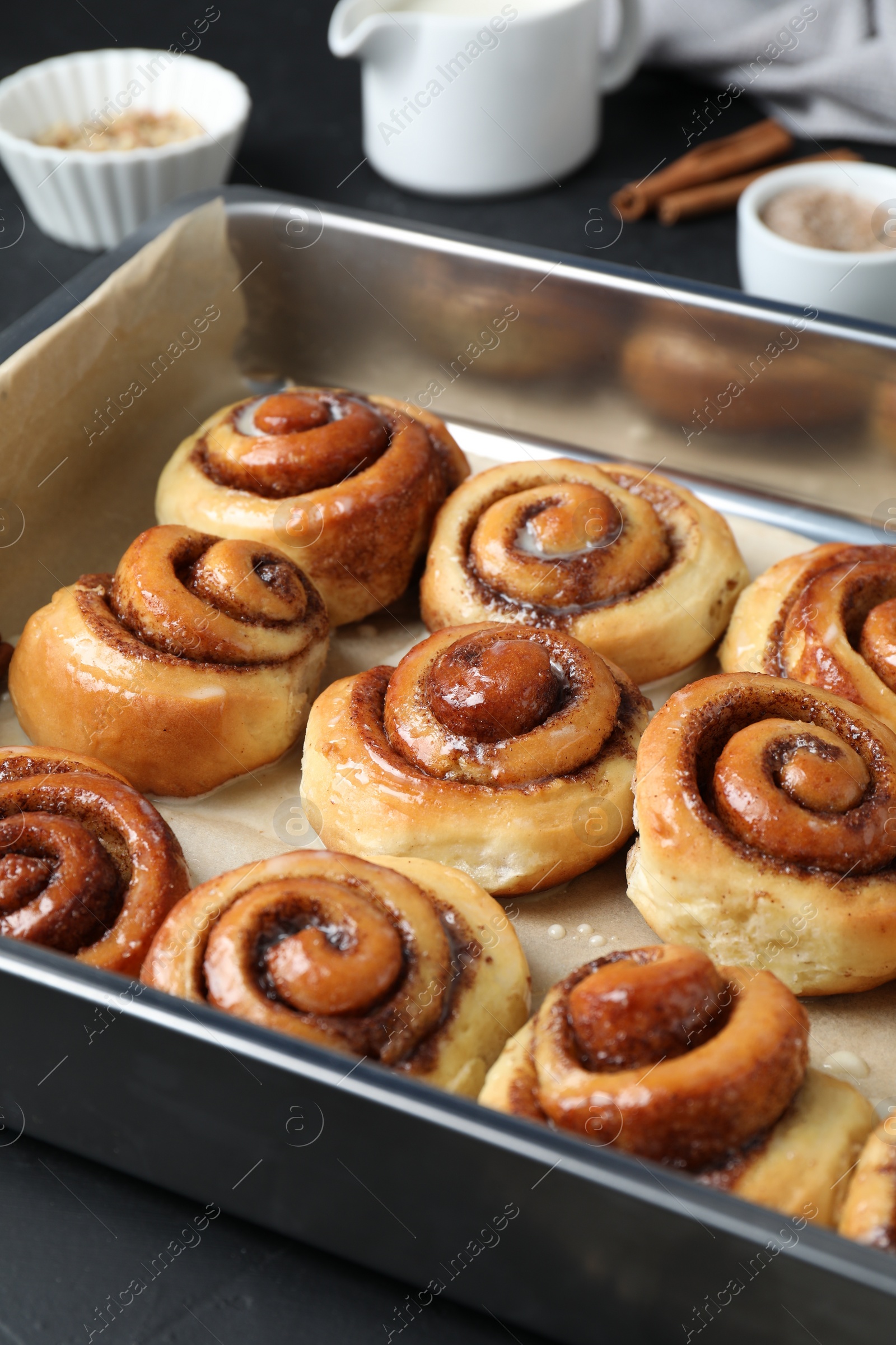 Photo of Baking dish with tasty cinnamon rolls on dark table