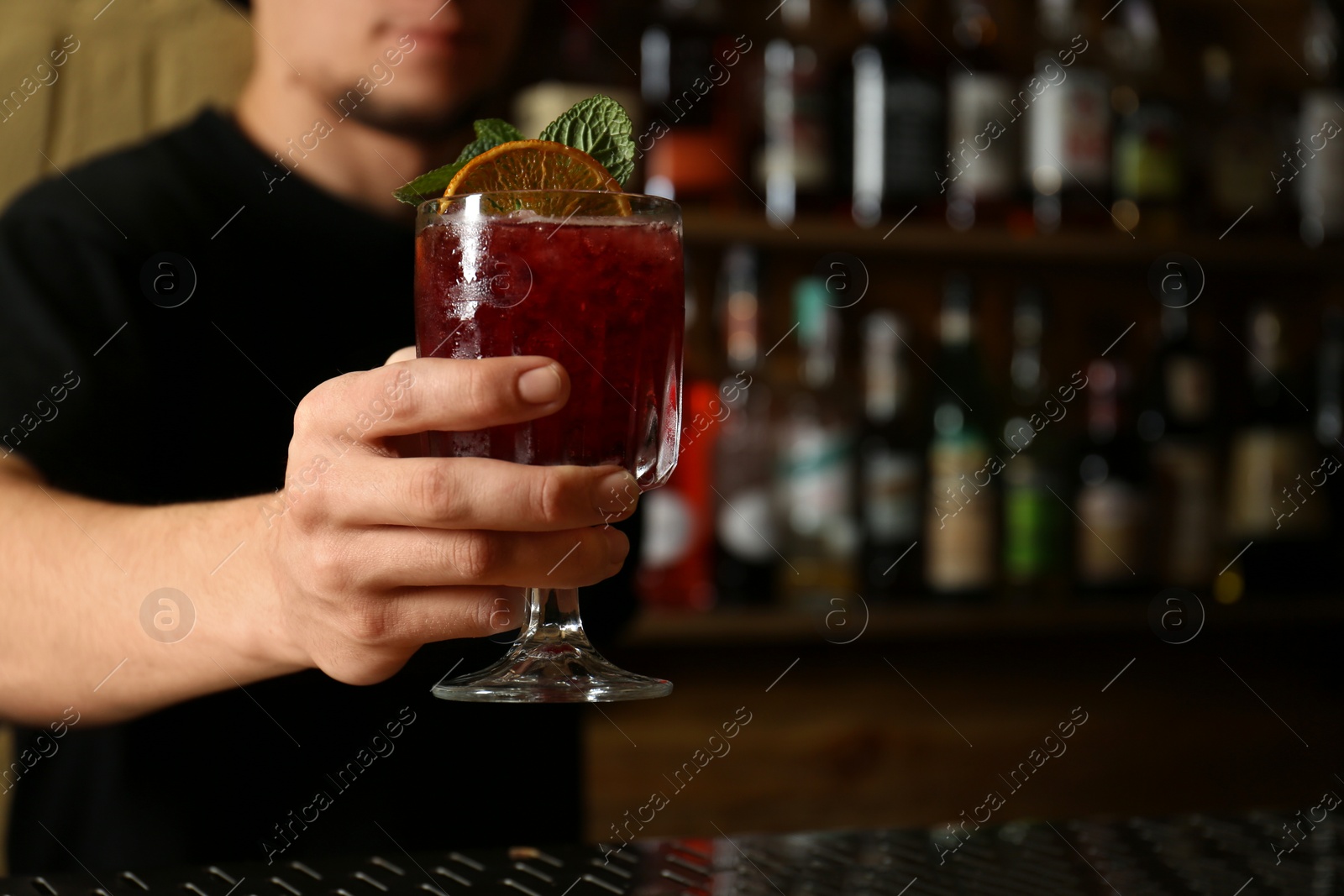 Photo of Bartender holding glass of fresh alcoholic cocktail in bar, closeup. Space for text
