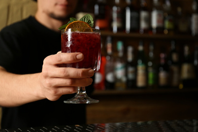 Photo of Bartender holding glass of fresh alcoholic cocktail in bar, closeup. Space for text