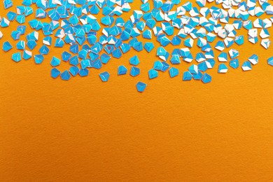 Photo of Shiny bright light blue glitter on orange background. Space for text