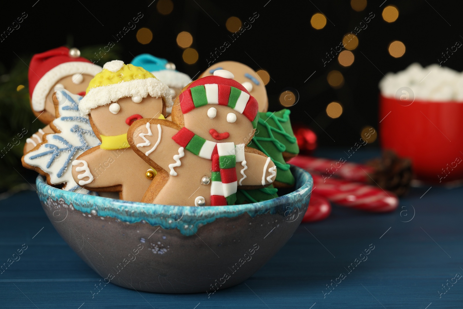 Photo of Delicious homemade Christmas cookies in bowl on blue wooden table against blurred festive lights. Space for text
