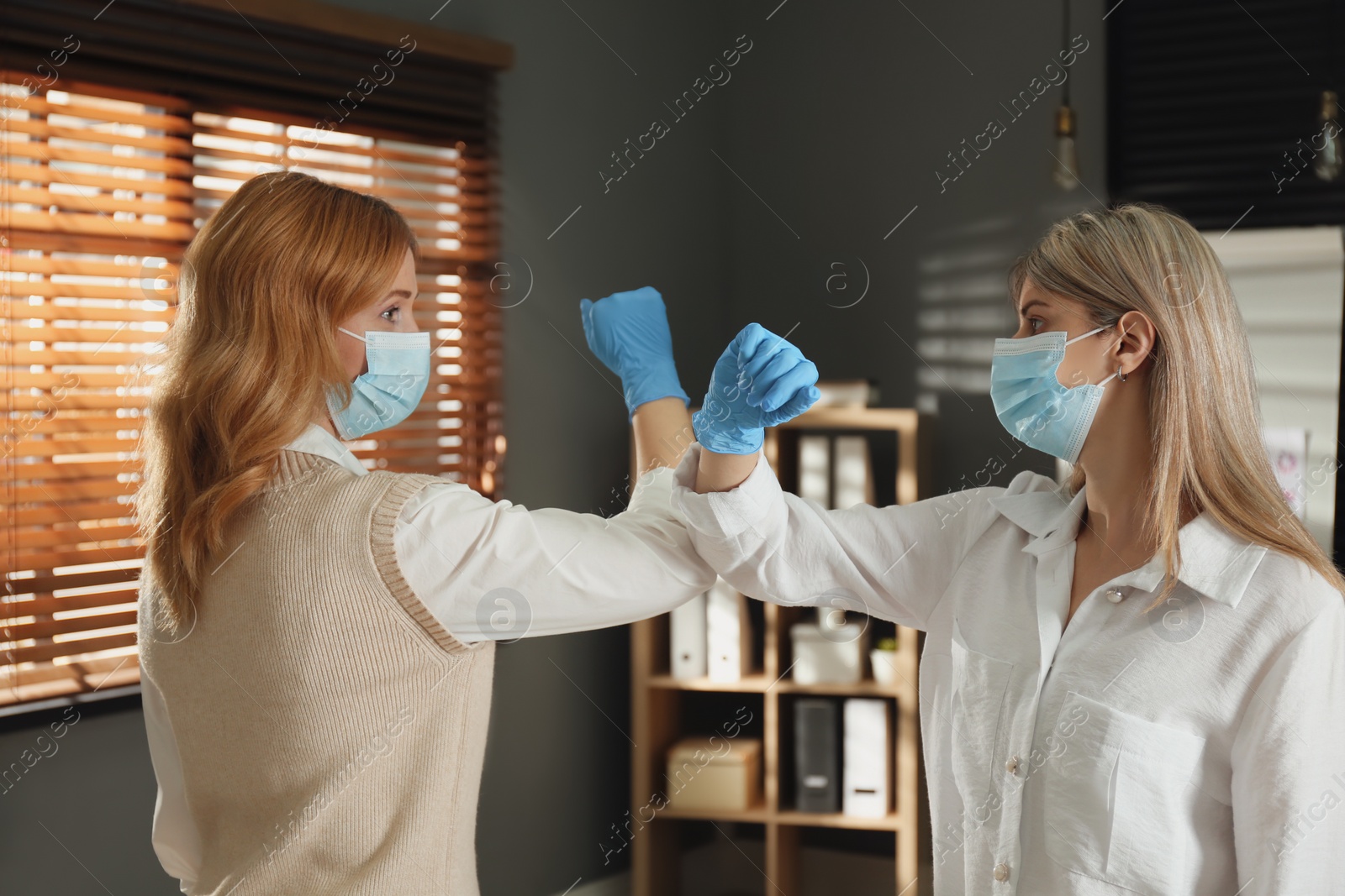 Photo of People greeting each other by bumping elbows instead of handshake indoors