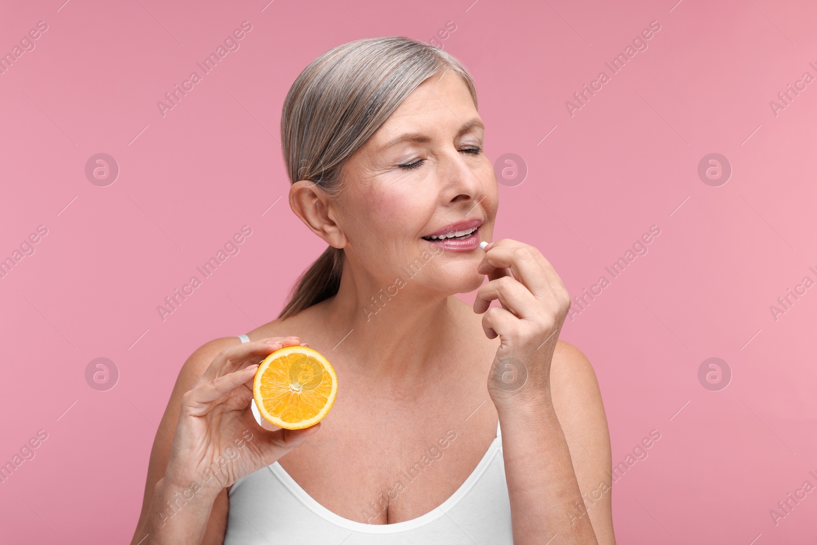 Photo of Beautiful woman with half of orange taking vitamin capsule on pink background