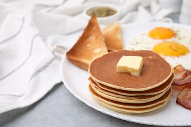 Photo of Tasty pancakes with fried eggs and bacon on grey table, closeup. Space for text