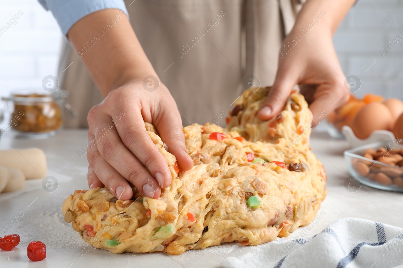 Photo of Woman kneading dough with candied fruits and nuts for Stollen at white table, closeup. Baking traditional German Christmas bread