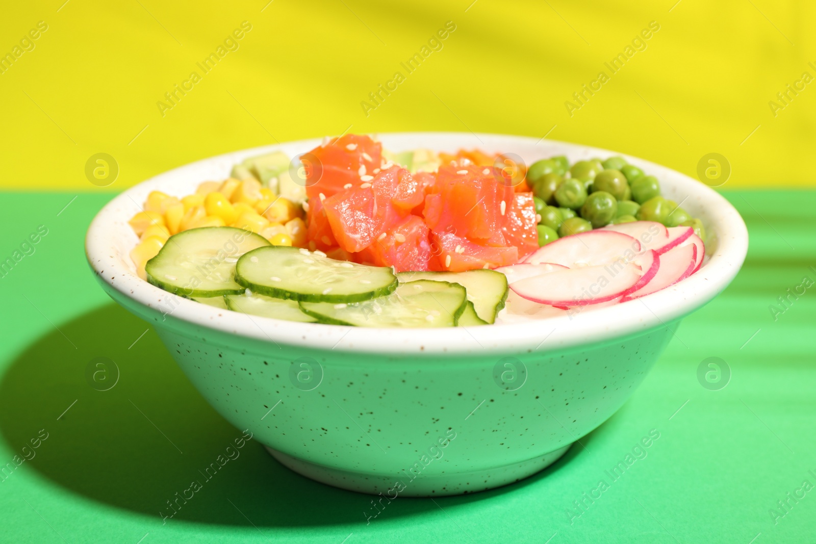 Photo of Delicious salad with salmon and vegetables in bowl on color background
