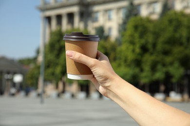 Photo of Woman holding takeaway cardboard coffee cup with plastic lid outdoors, closeup