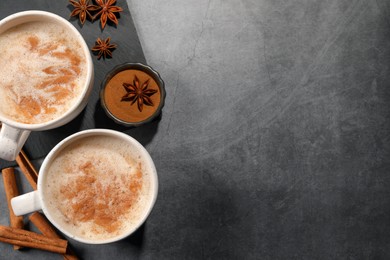 Cups of delicious eggnog with anise and cinnamon on grey table, flat lay. Space for text