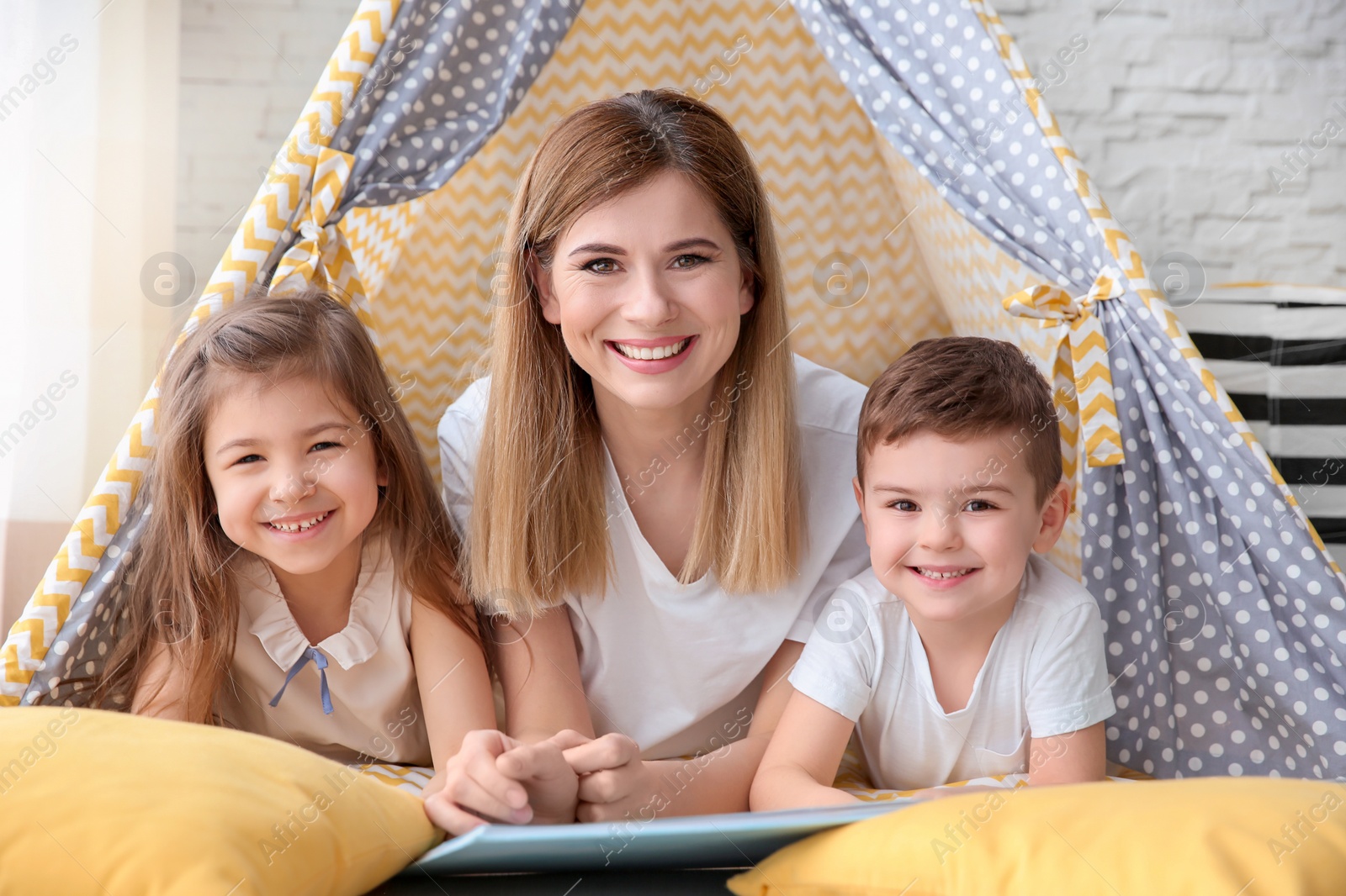 Photo of Nanny and little children reading book in tent at home