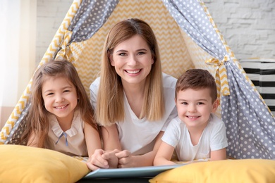 Nanny and little children reading book in tent at home