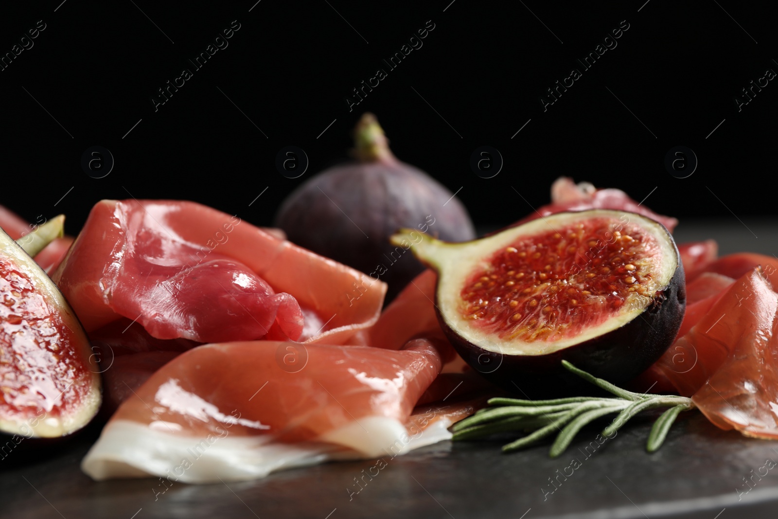 Photo of Delicious ripe figs and prosciutto served on black table, closeup