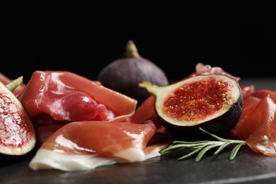 Photo of Delicious ripe figs and prosciutto served on black table, closeup