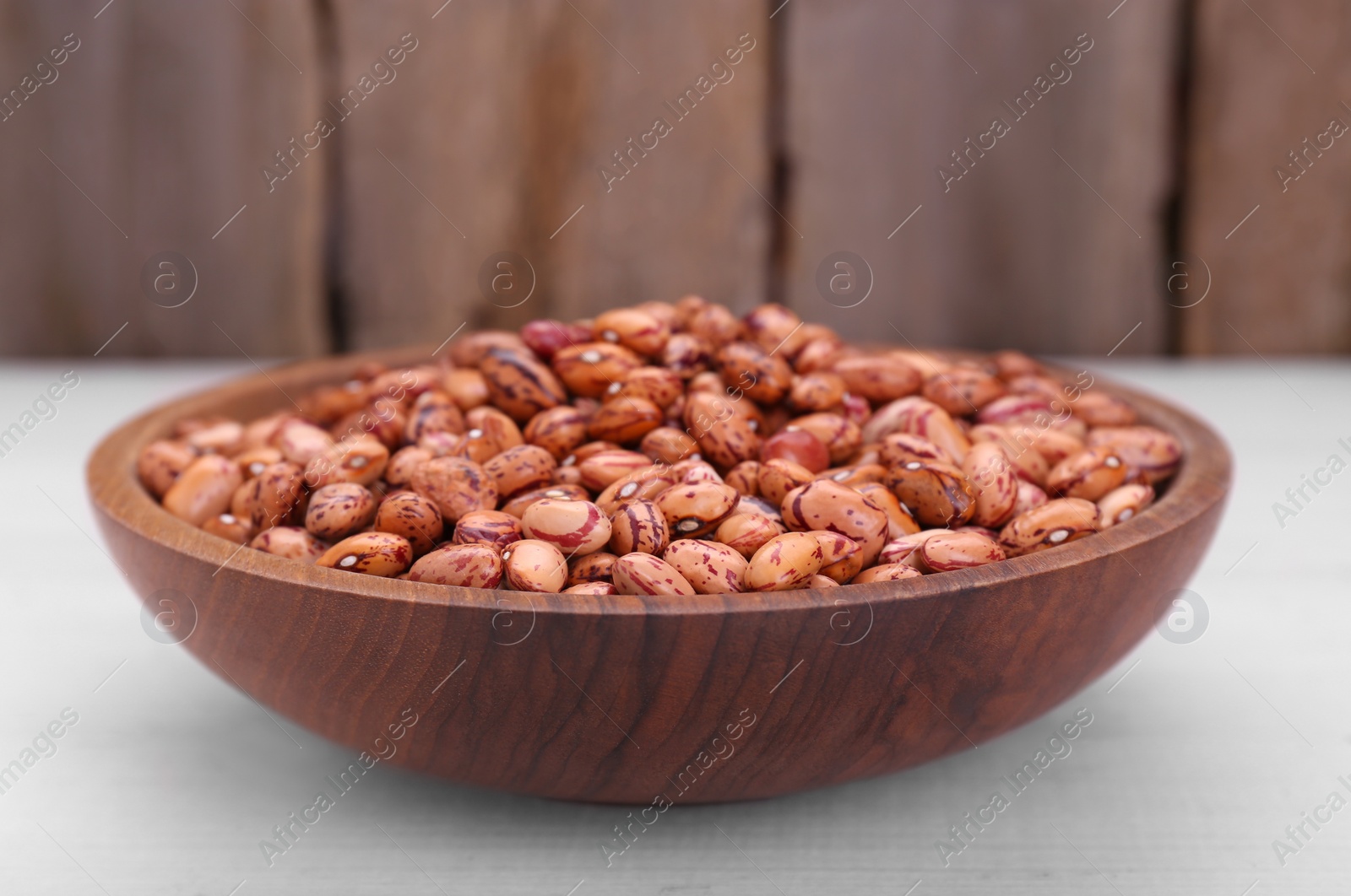 Photo of Bowl with dry kidney beans on white wooden table, closeup