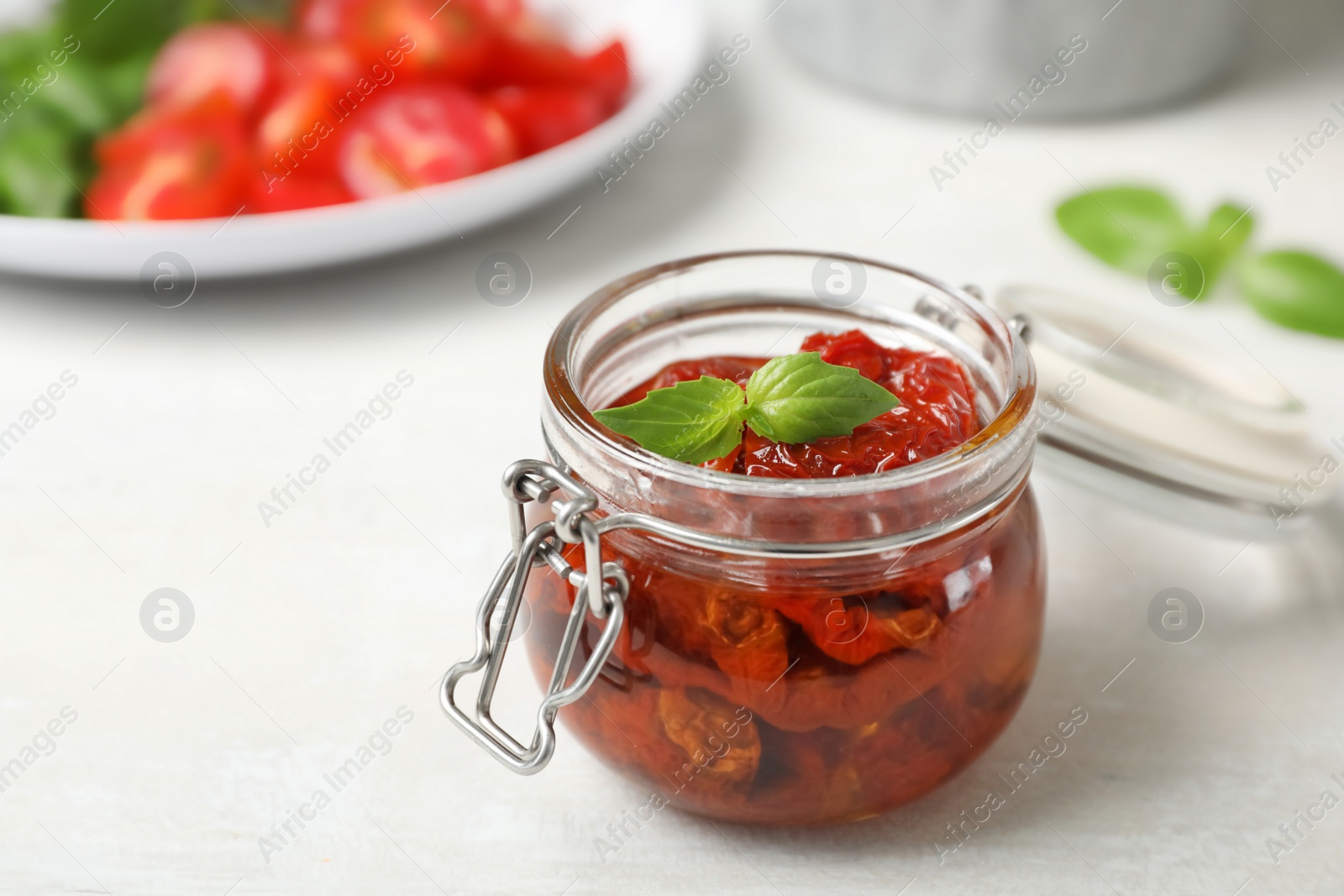 Photo of Jar with sun dried tomatoes on light table. Space for text