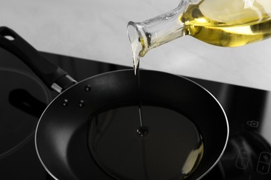Photo of Pouring cooking oil from jug into frying pan on stove, closeup