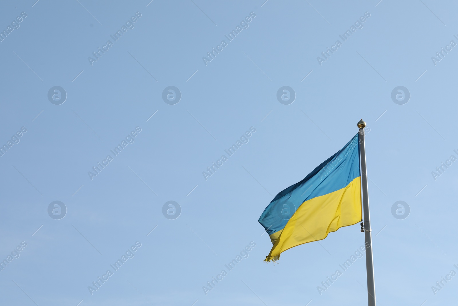 Photo of Flag of Ukraine waving on pole against blue sky. Space for text