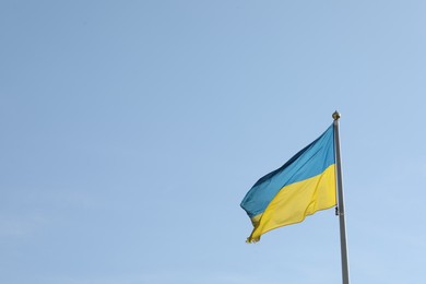 Photo of Flag of Ukraine waving on pole against blue sky. Space for text