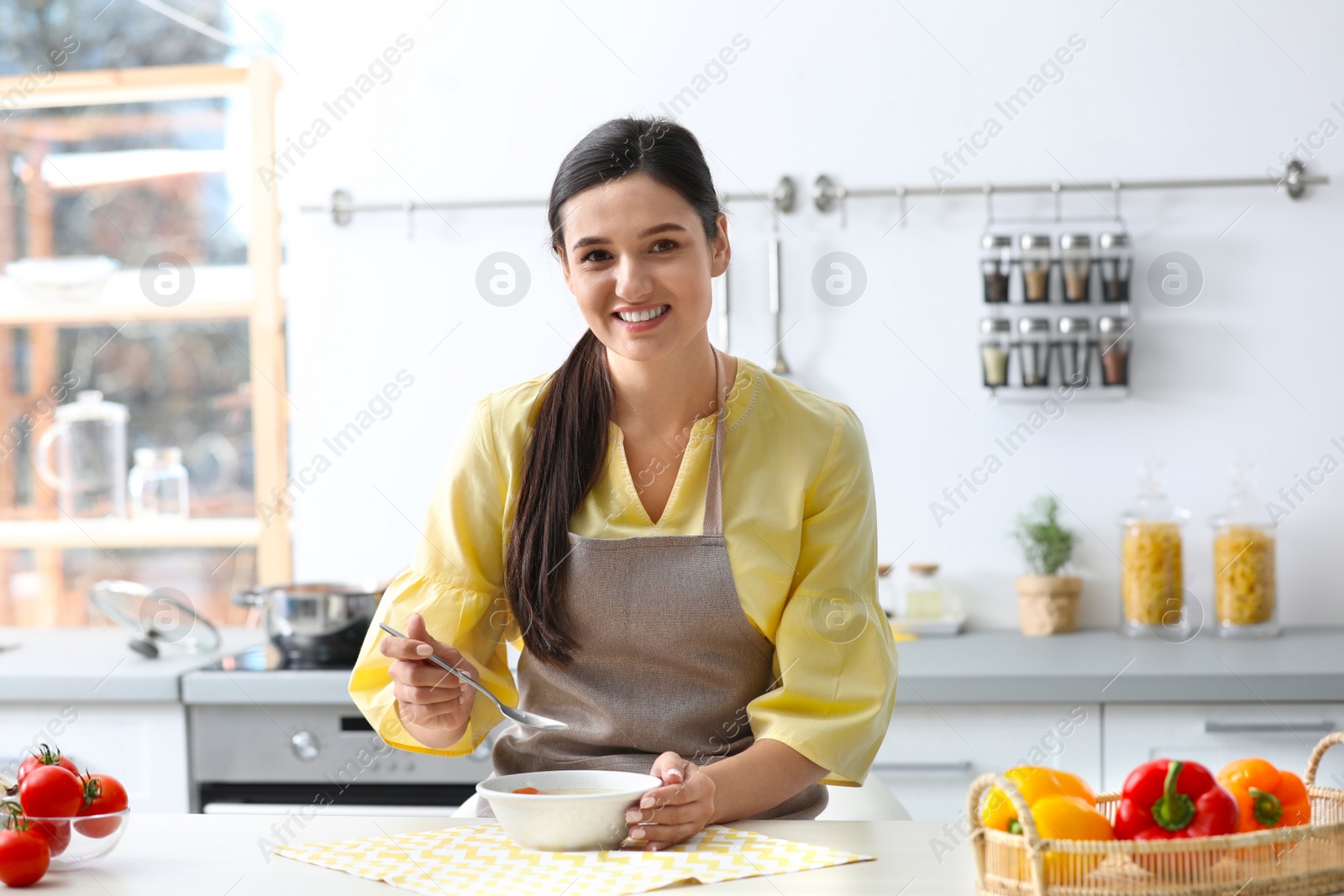 Photo of Young woman eating tasty vegetable soup at table in kitchen