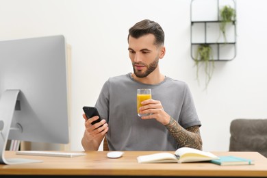 Handsome man with delicious smoothie and smartphone at workplace in office