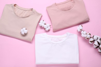 Cotton branch with fluffy flowers and t-shirts on pink background, flat lay