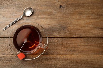 Photo of Tea bag in glass cup of hot water on wooden table, flat lay. Space for text