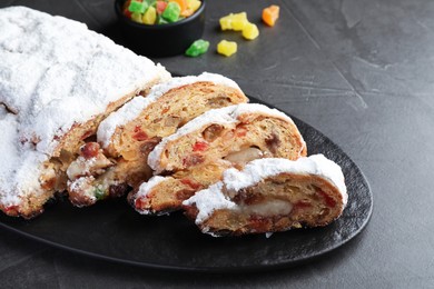 Traditional Christmas Stollen with icing sugar on black table, closeup