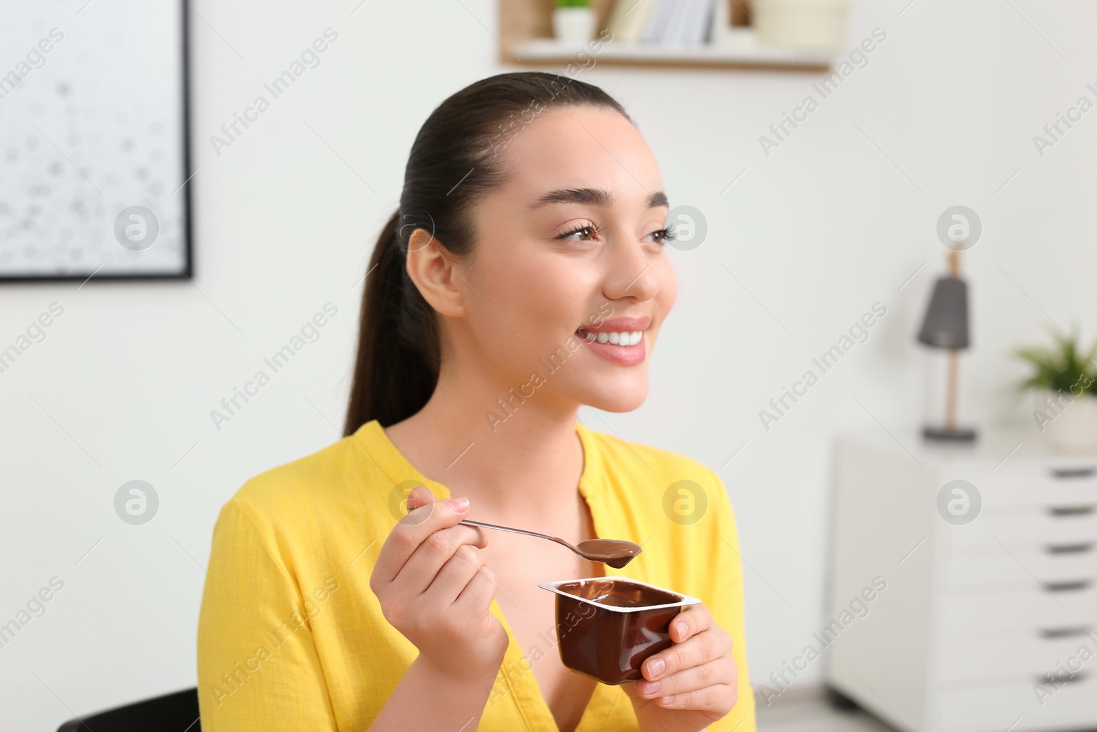 Photo of Happy woman with tasty yogurt at home