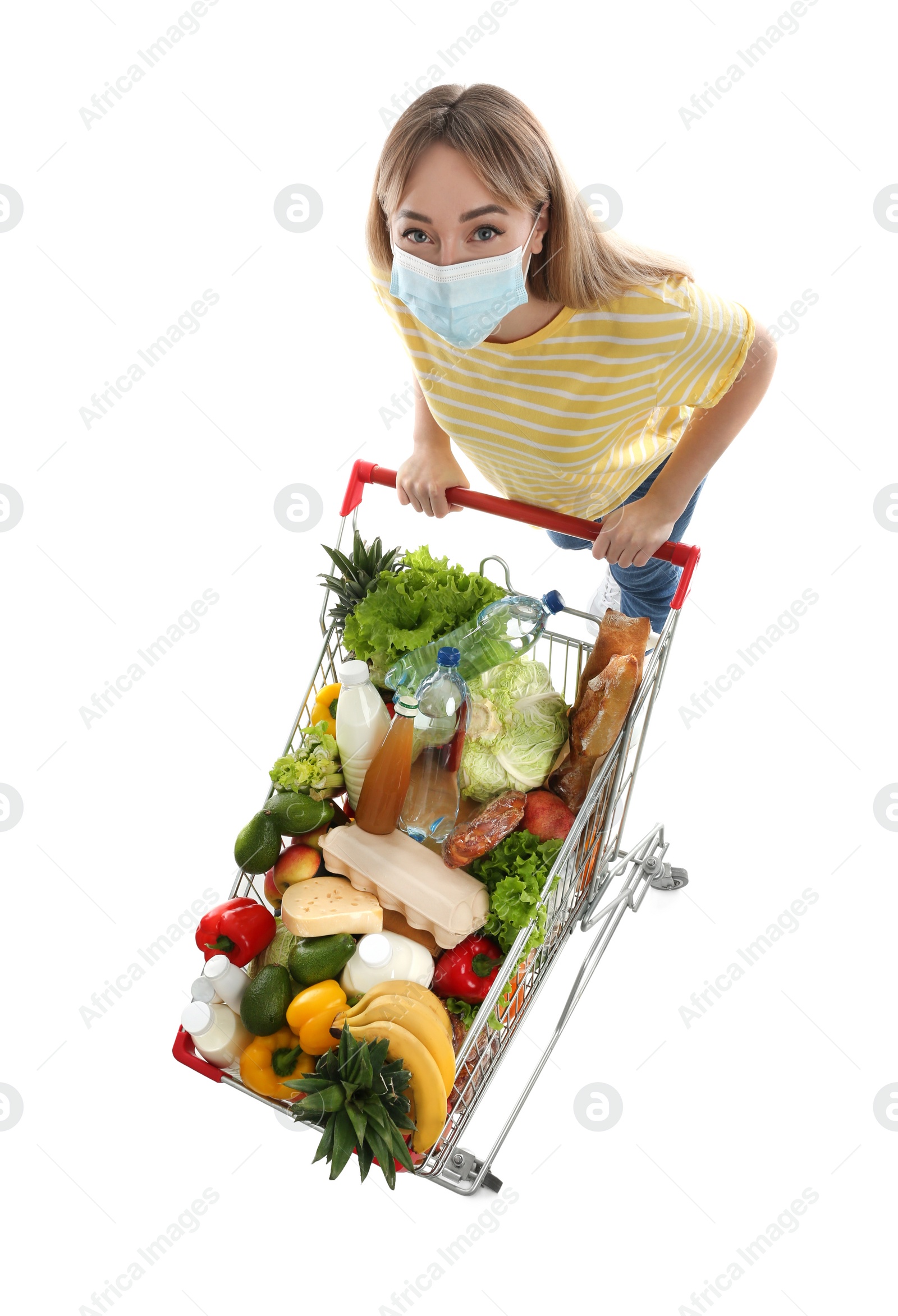 Photo of Young woman in medical mask with shopping cart full of groceries on white background, above view
