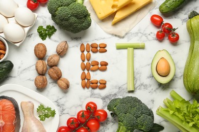 Photo of Word Keto made of products surrounded by other food on white marble table, flat lay