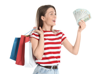 Emotional young woman with money and shopping bags on white background