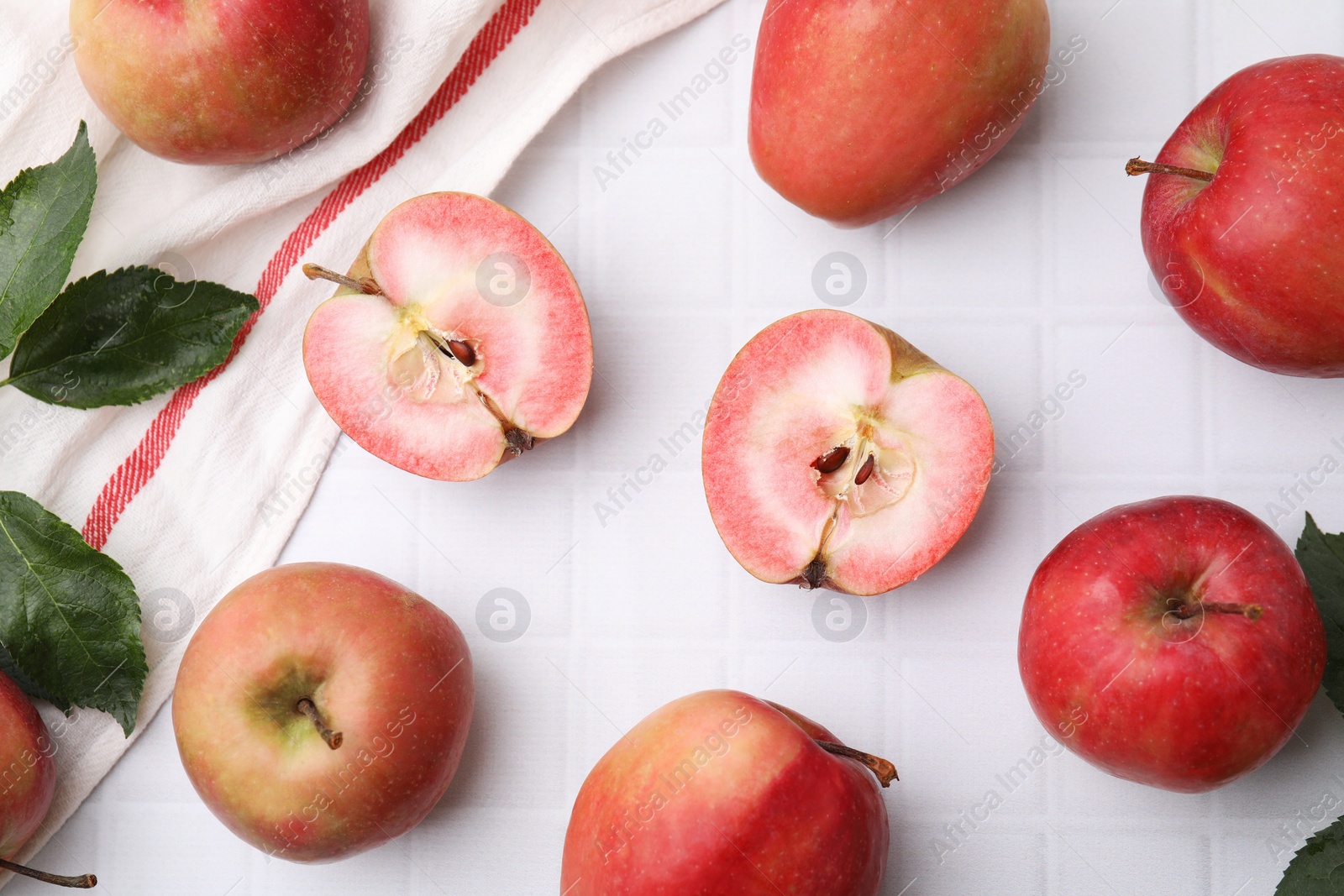 Photo of Tasty apples with red pulp and leaves on white tiled table, flat lay