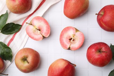 Tasty apples with red pulp and leaves on white tiled table, flat lay