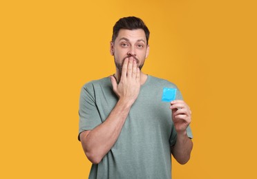Photo of Confused man holding condom on orange background