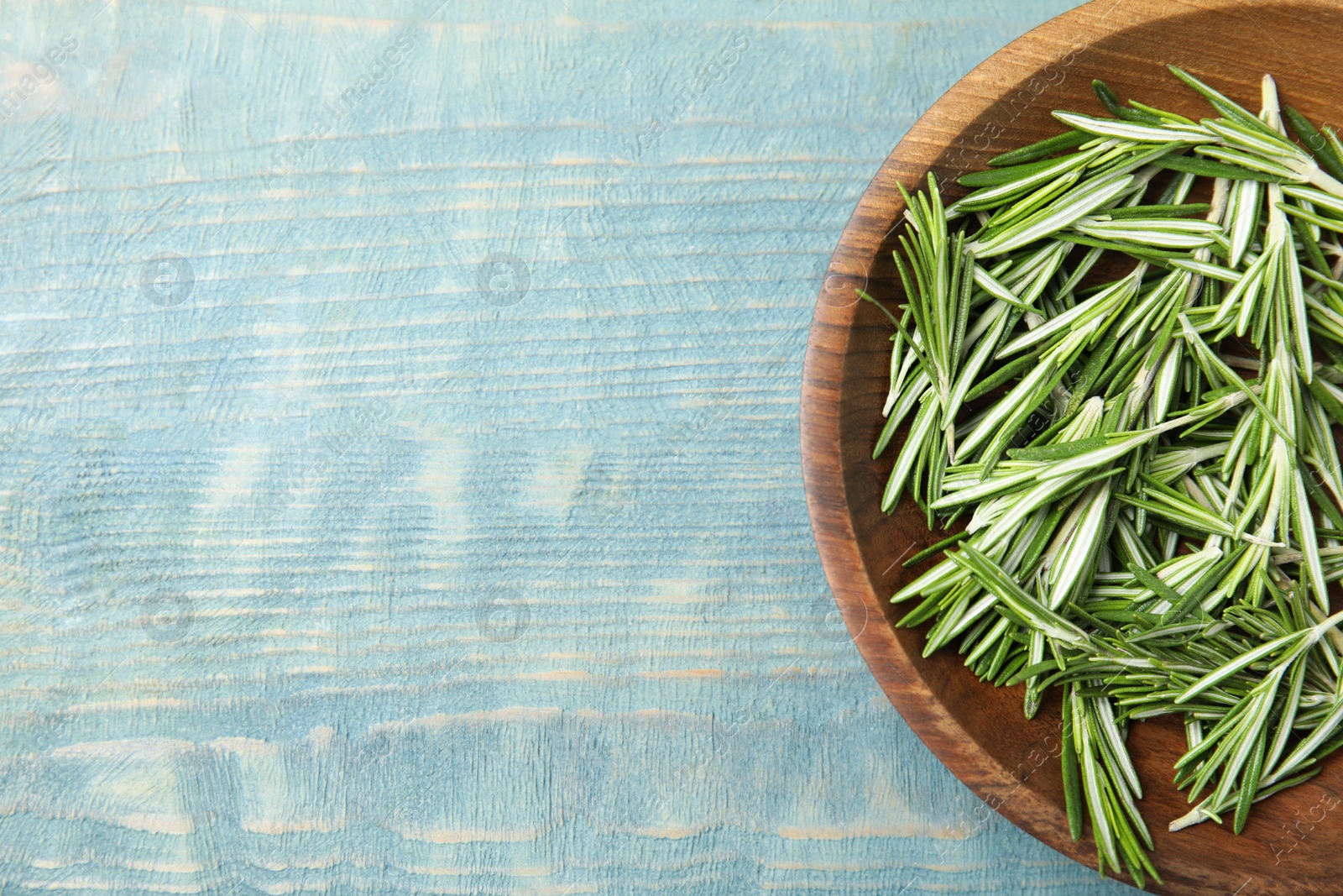 Photo of Wooden bowl with fresh rosemary on color table, flat lay. Space for text