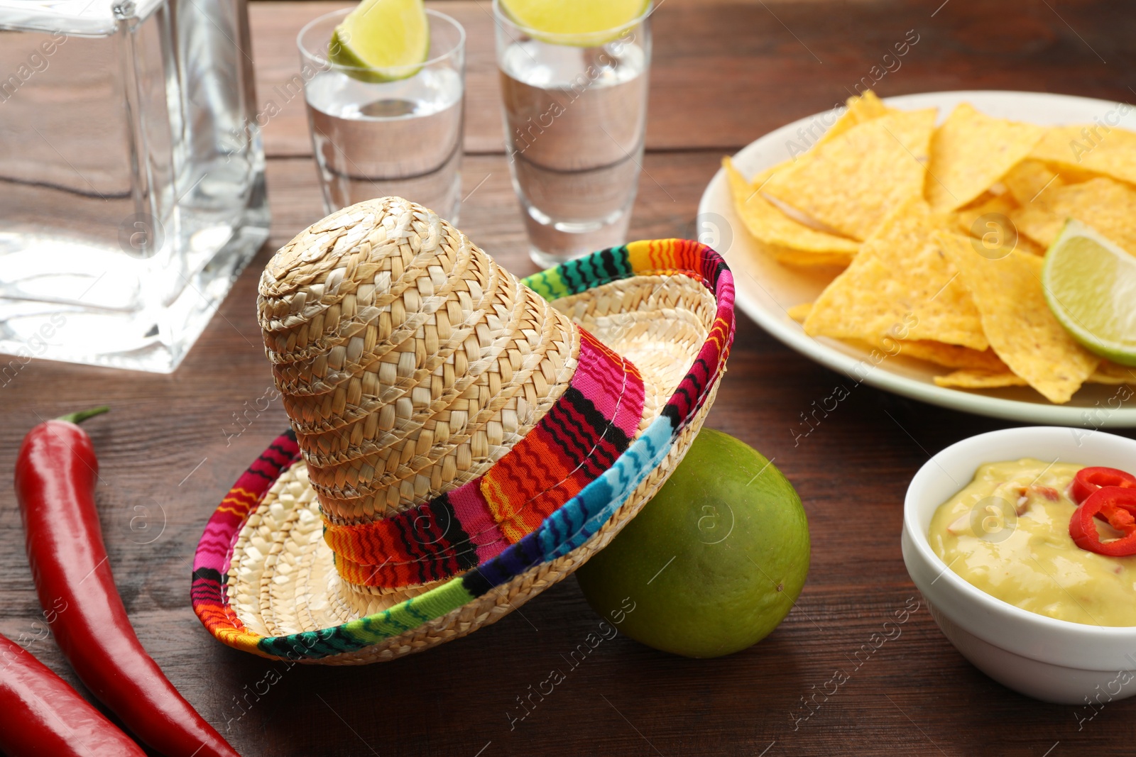 Photo of Mexican sombrero hat, tequila with lime, chili peppers, nachos chips and dip sauce on wooden table