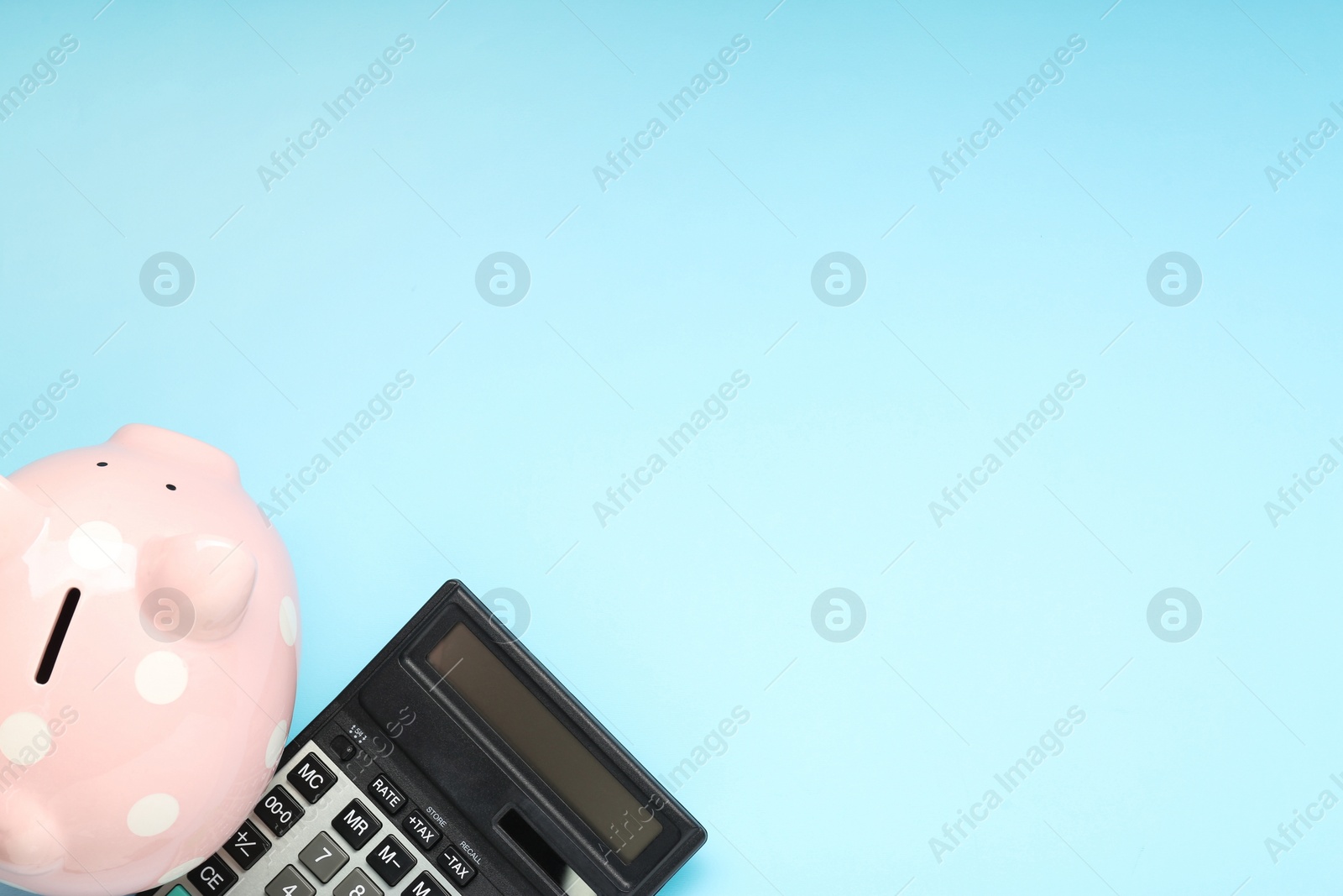 Photo of Calculator and piggy bank on light blue background, top view. Space for text