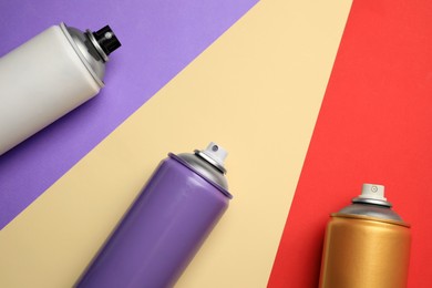 Cans of different spray paints on color background, flat lay with space for text. Graffiti supplies