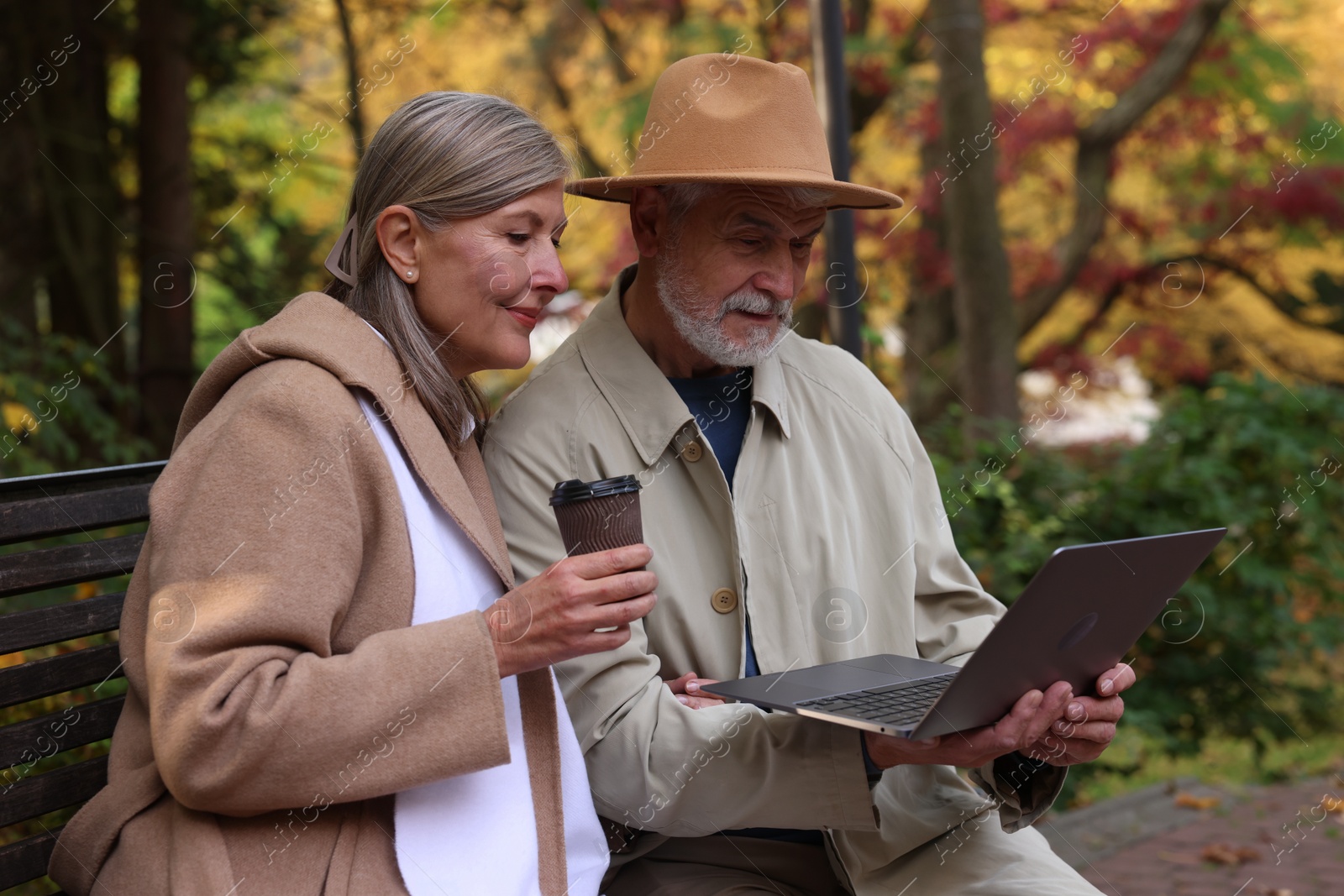 Photo of Affectionate senior couple with laptop spending time together in autumn park