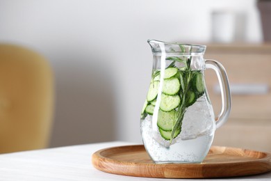 Photo of Refreshing cucumber water with rosemary in jug on white table. Space for text