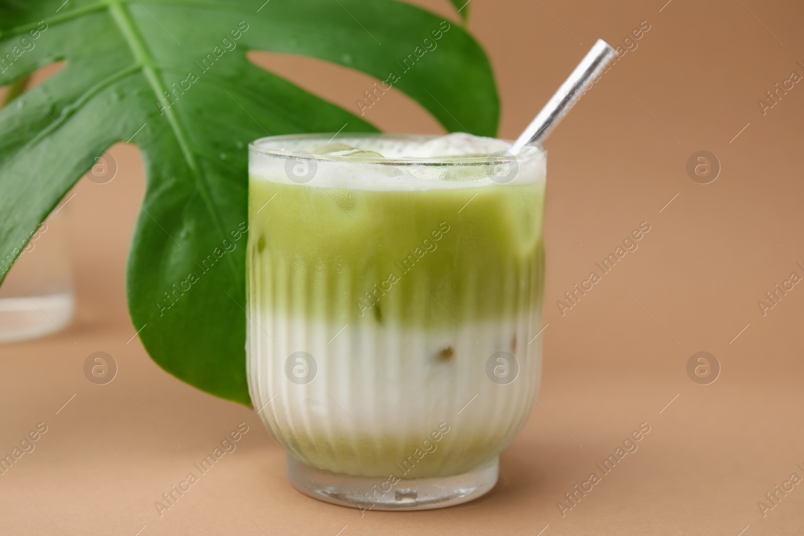 Photo of Glass of tasty iced matcha latte and leaf on light brown background, closeup